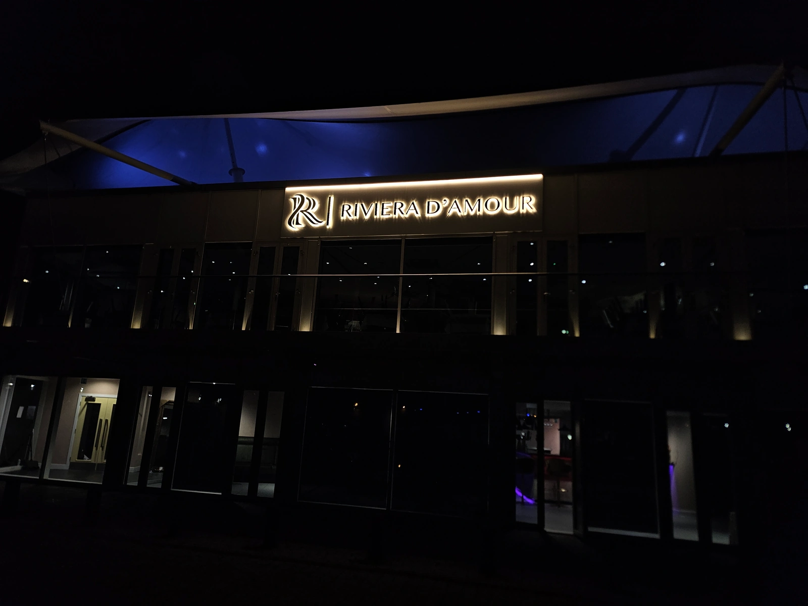 Riviera D'Amour fascia lettering and monogram with warm halo illumination at night